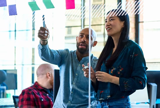 A man and a woman in an office,  planning with sticky notes on a glass wall