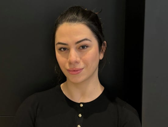 Women wearing a black top is standing against a dark background.