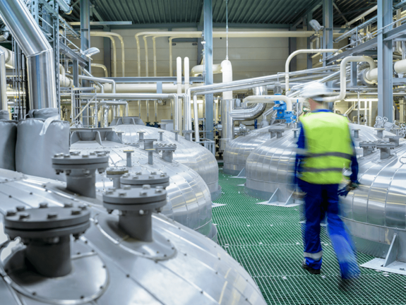 man with yellow jacket and white helmet, walking in a factory