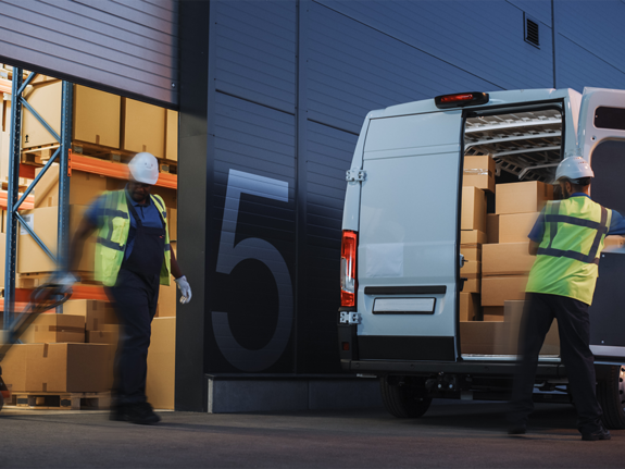 hommes déplaçant un chariot élévateur rempli de cartons à charger dans une camionnette