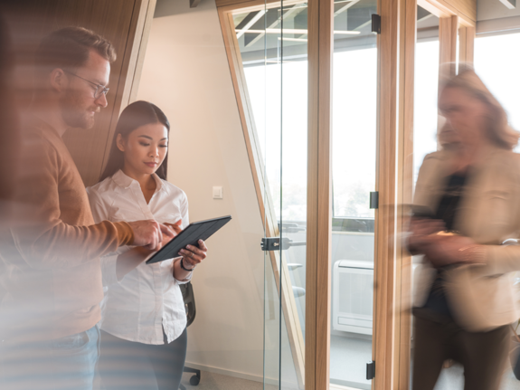 woman looking at a tablet in an office with people walking around her